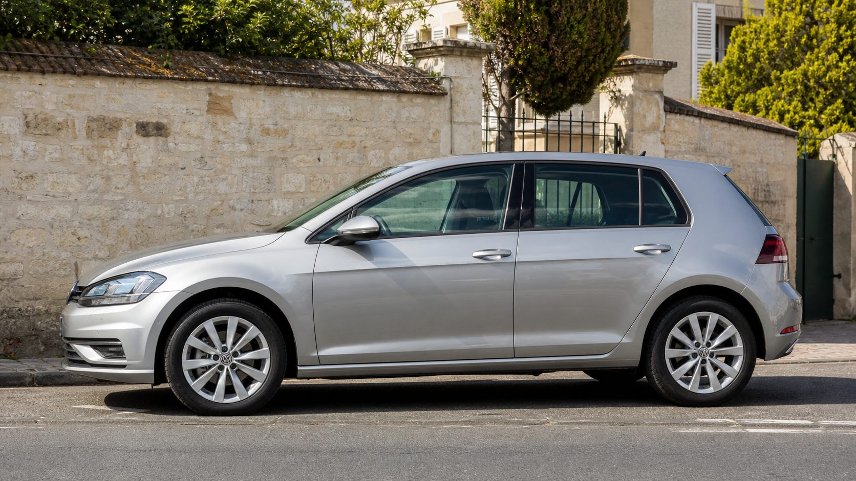 Silberner Volkswagen Golf auf sonniger Straße geparkt